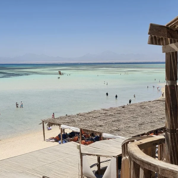 Zicht vanaf een houten strandterras op ondiep water en bezoekers bij Orange Bay