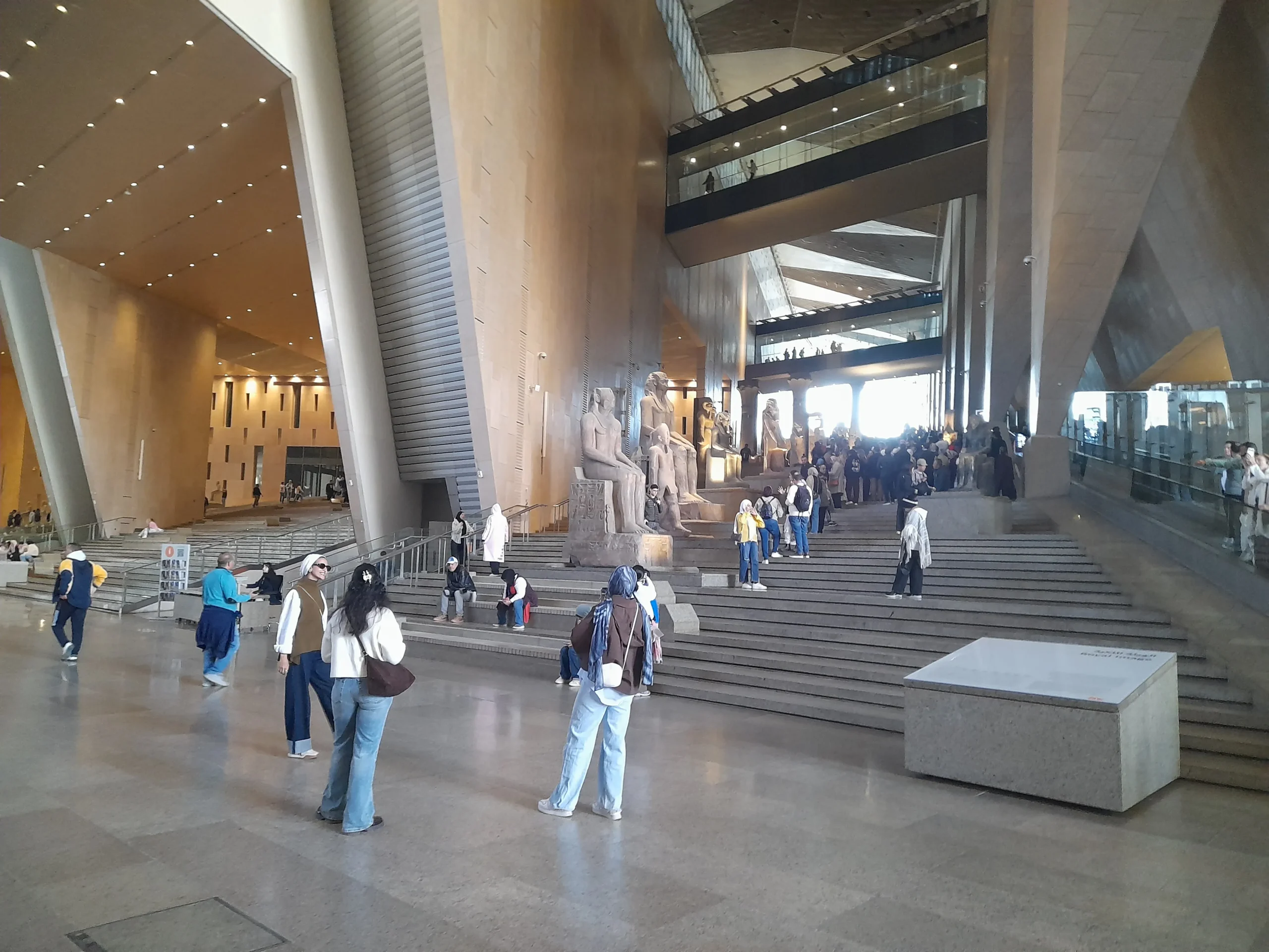 De Grote Trap en het atrium van het Grand Egyptian Museum met farao-beelden en bezoekers
