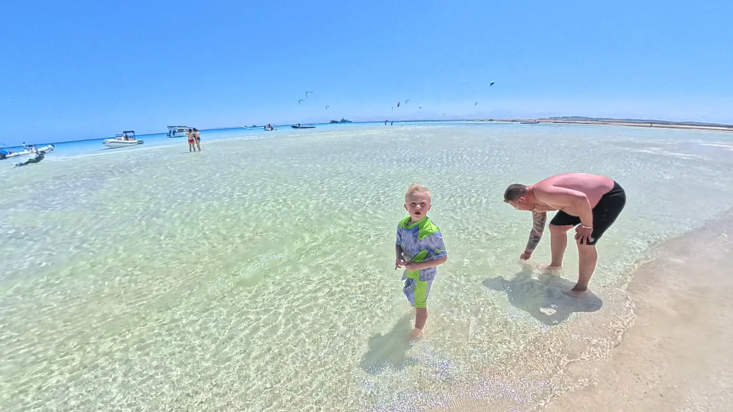 Ouder en kind spelen in het ondiepe heldere water op de zandbank van Orange Bay bij Hurghada