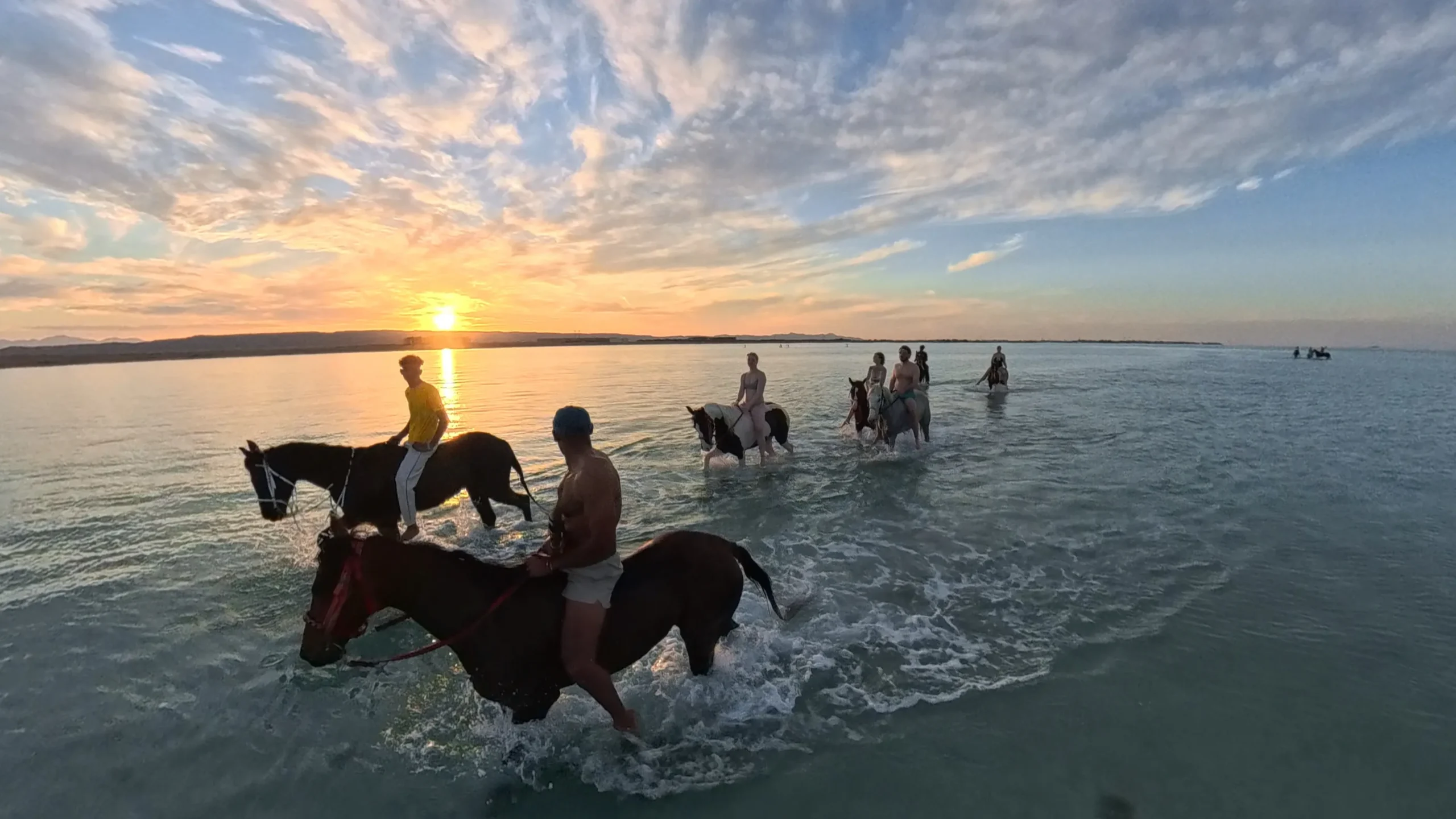 Paardrijden Hurghada: mensen rijden te paard door het ondiepe zeewater bij een gouden zonsondergang op het strand